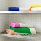 Colorful towels stacked on a shelf against a tiled wall.