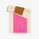A folded face towel with hot pink and chestnut brown stripes on a beige background, with a loop for hanging.