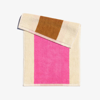 A folded face towel with hot pink and chestnut brown stripes on a beige background, with a loop for hanging.