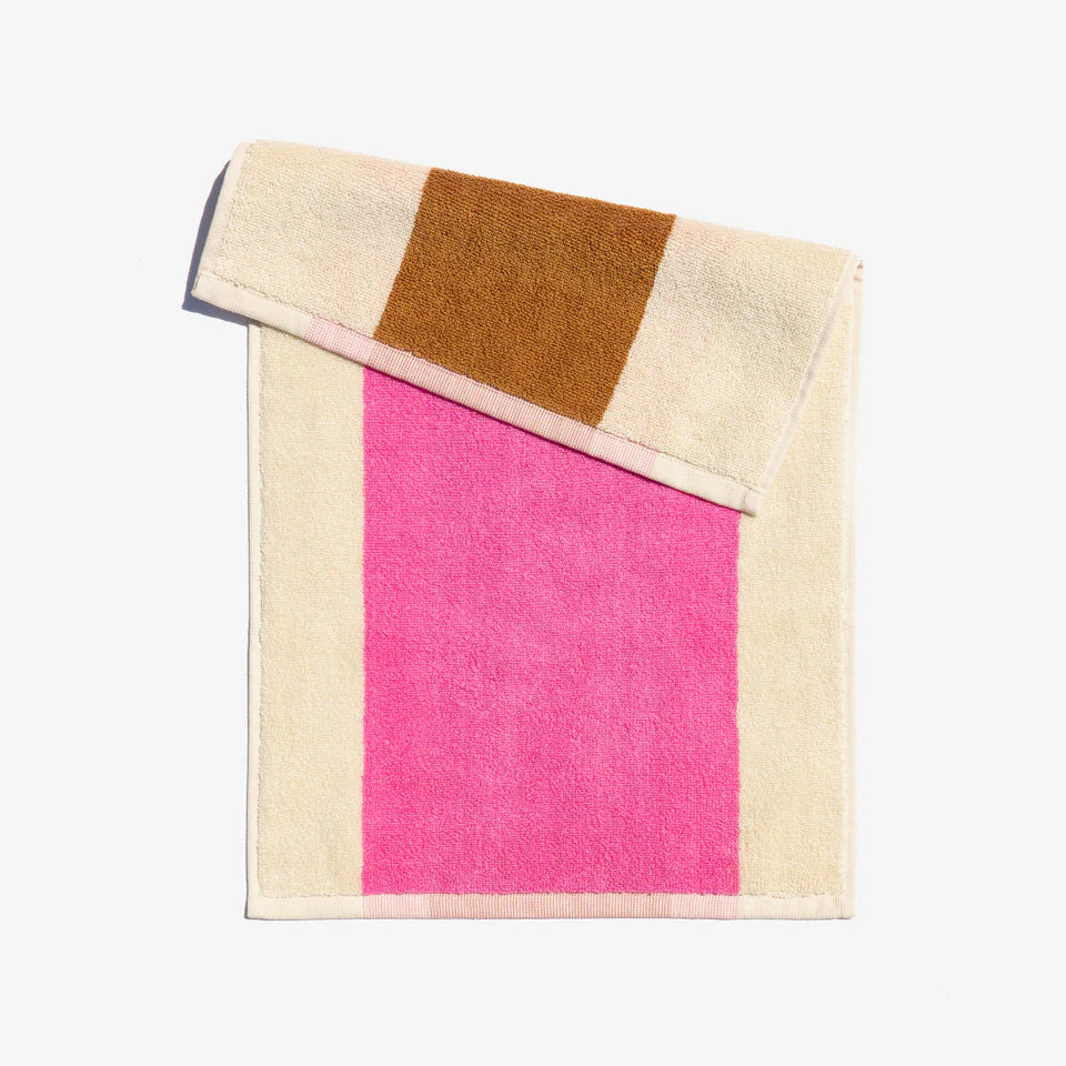 A folded face towel with hot pink and chestnut brown stripes on a beige background, with a loop for hanging.