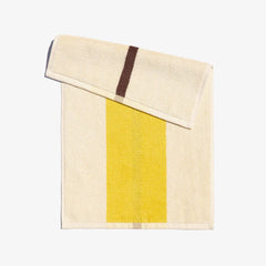 A folded face towel with a lemon yellow and coffee brown stripe design on a light background, displayed on a neutral surface.