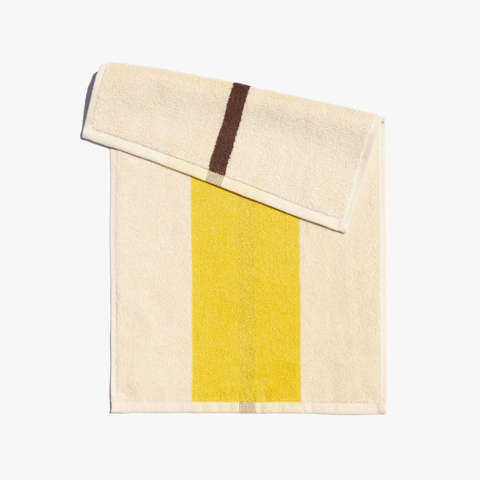 A folded face towel with a lemon yellow and coffee brown stripe design on a light background, displayed on a neutral surface.