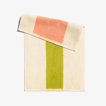A folded face towel with peach and lime green horizontal stripes on a light background, with a loop for hanging.