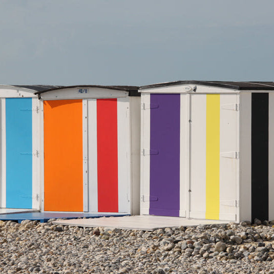 Colorful striped beach huts on a pebbly beach with a clear sky.