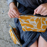 A woman zipping up the yellow print patterned wash bag on her laps.