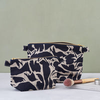 Two navy blue patterned linen wash bags in two sizes and a make up brush laying on the book next to.