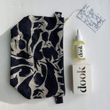 A folded, lying flat navy blue, patterned linen wash bag next to dook's products - conditioning oil and bar of soap in a box.