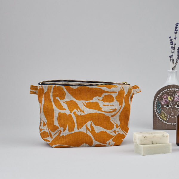 An open, yellow print patterned linen wash bag standing next to bar of soaps and a decorative vase.