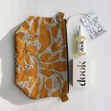A composition from the top of a yellow print patterned linen wash bag lying flat next to dook's products - a boxed soap and a conditioning oil.