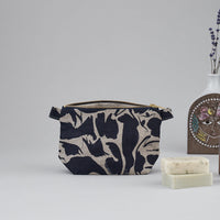 Small navy blue patterned linen wash bag with an open zip standing next to two unboxed bar of soaps and a decorative vase.
